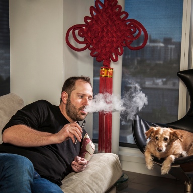 portrait photography of Jan Verleur vaping on a sofa with his dog nearby